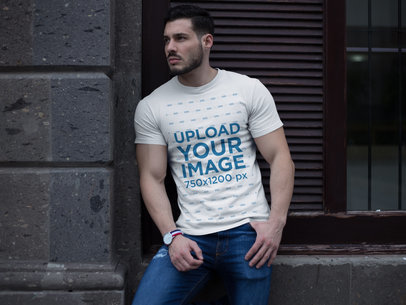 Buff Man Wearing a T-Shirt Mockup While Lying Against a Wall