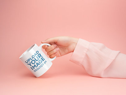 Mockup of a Woman's Hand Holding a Coffee Mug Against a Pale Pink Background