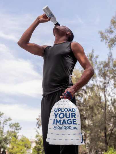 Mockup of a Man Drinking Water from an Aluminium Bottle while Holding a Drawstring Bag 