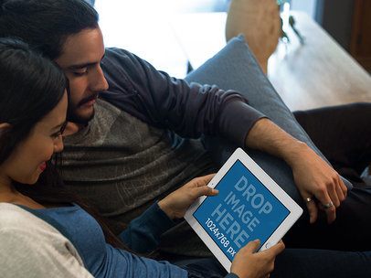 White iPad Mockup in Landscape Position of a Couple Lying on a Couch in their Apartment a13103