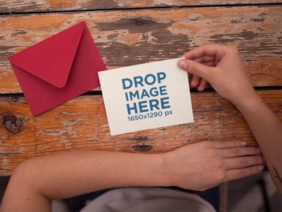 Invitation Template Held Near a Red Envelope on an Old Wooden Table a14750